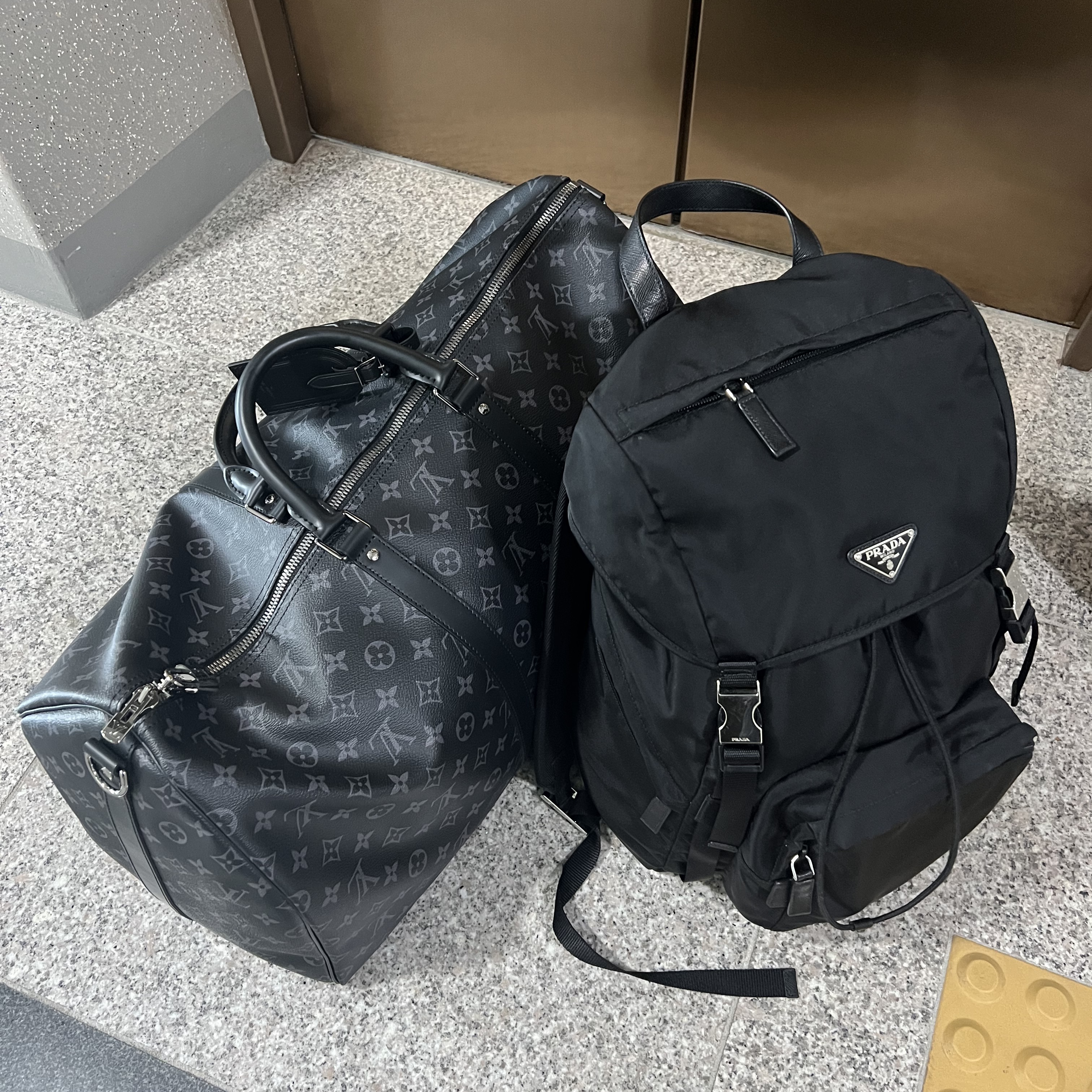 Louis Vuitton Keepall Bandouliere 55 Monogram Eclipse Grey, Prada Re-Nylon and Saffiano Leather Backpack Black 착용 스타일